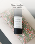A bottle of Spritz Wellness London Yoga Mat Spray placed on top of a floral-patterned mat, with promotional text above reading 'Rituals to enhance your practice'.