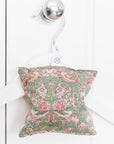 Decorative pillow with floral pattern hanging on a white wall.