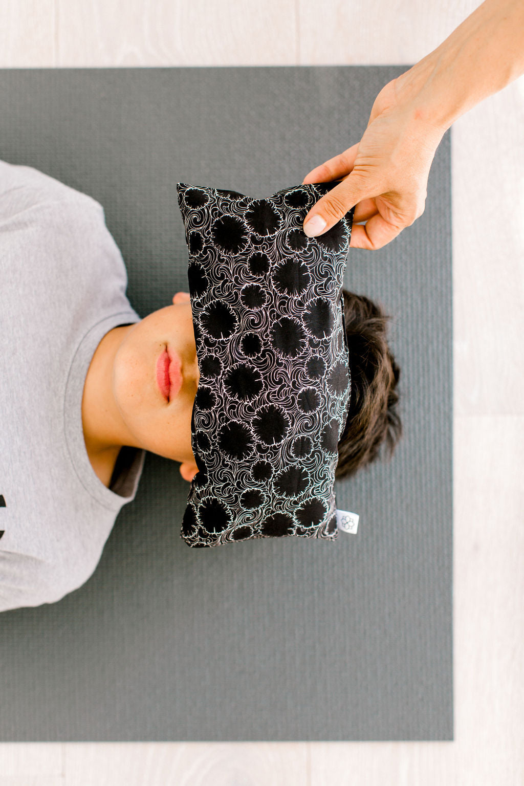 boy resting with and eye pillow with person placing the pillow over his eyes