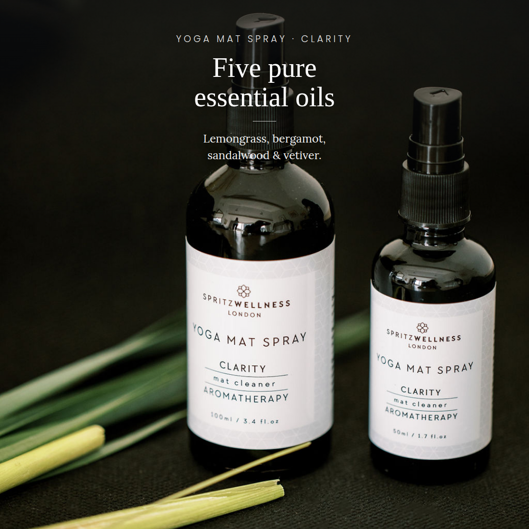 Two black glass bottles of Spritzwellness London essential oils on a dark background, with one bottle labeled 'Yoga Mat Spray Clarity' and the other partially visible. White text at the top reads 'Five pure essential oils' and lists the ingredients.