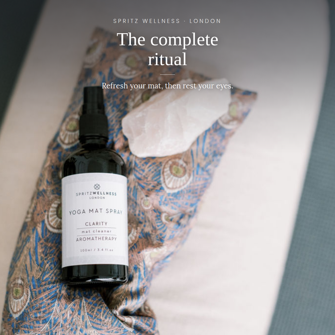 A bottle of Spritz Wellness London Yoga Mat Spray placed on a patterned blue and beige yoga mat next to a white crystal, with overlaid text reading 'The complete ritual' and 'Refresh your mat, then rest your eyes.'.