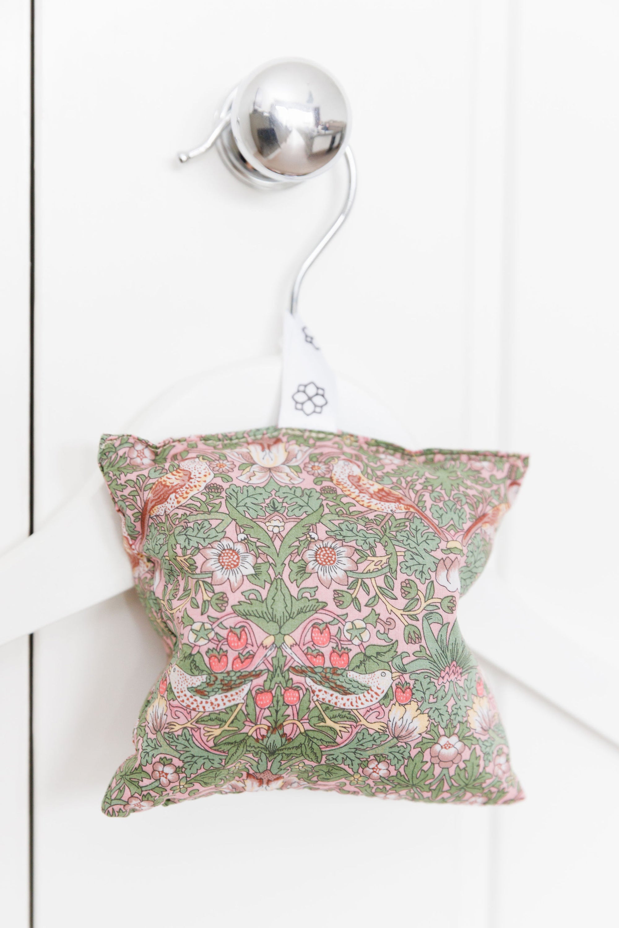 Decorative pillow with floral pattern hanging on a white wall.