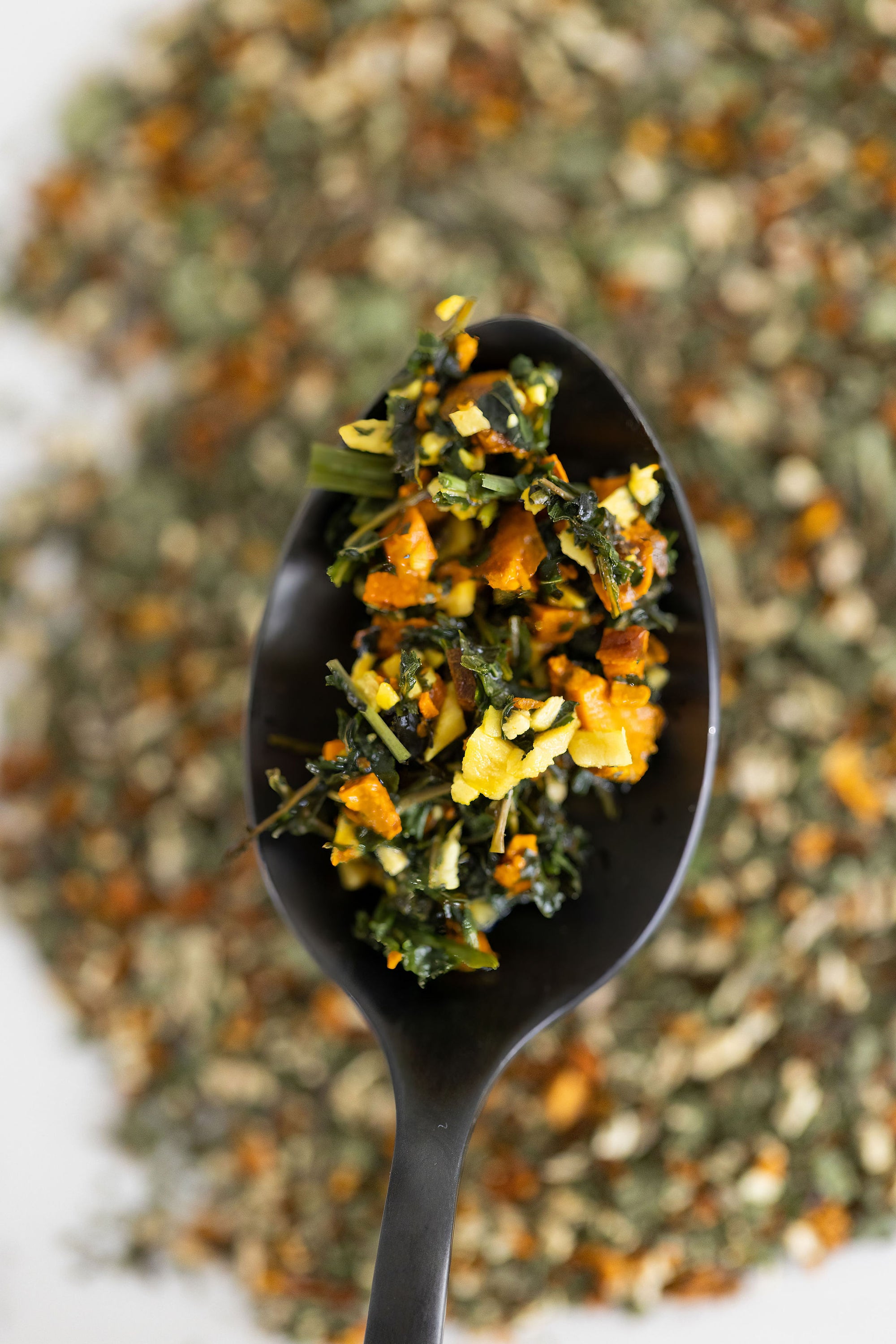 Black spoon filled with a mix of green and orange herbs against a blurred background