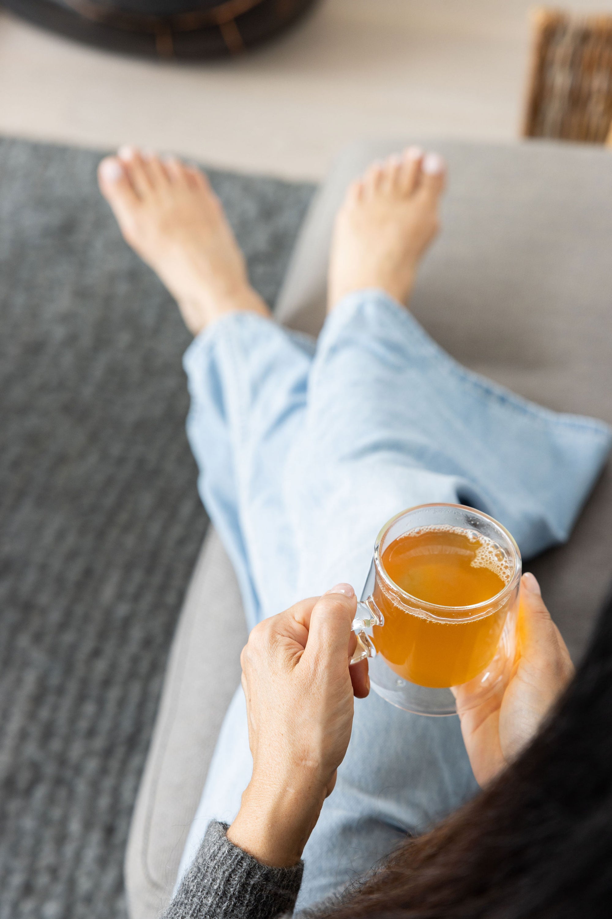 Person sitting on a couch holding a cup of golden Revive Tea