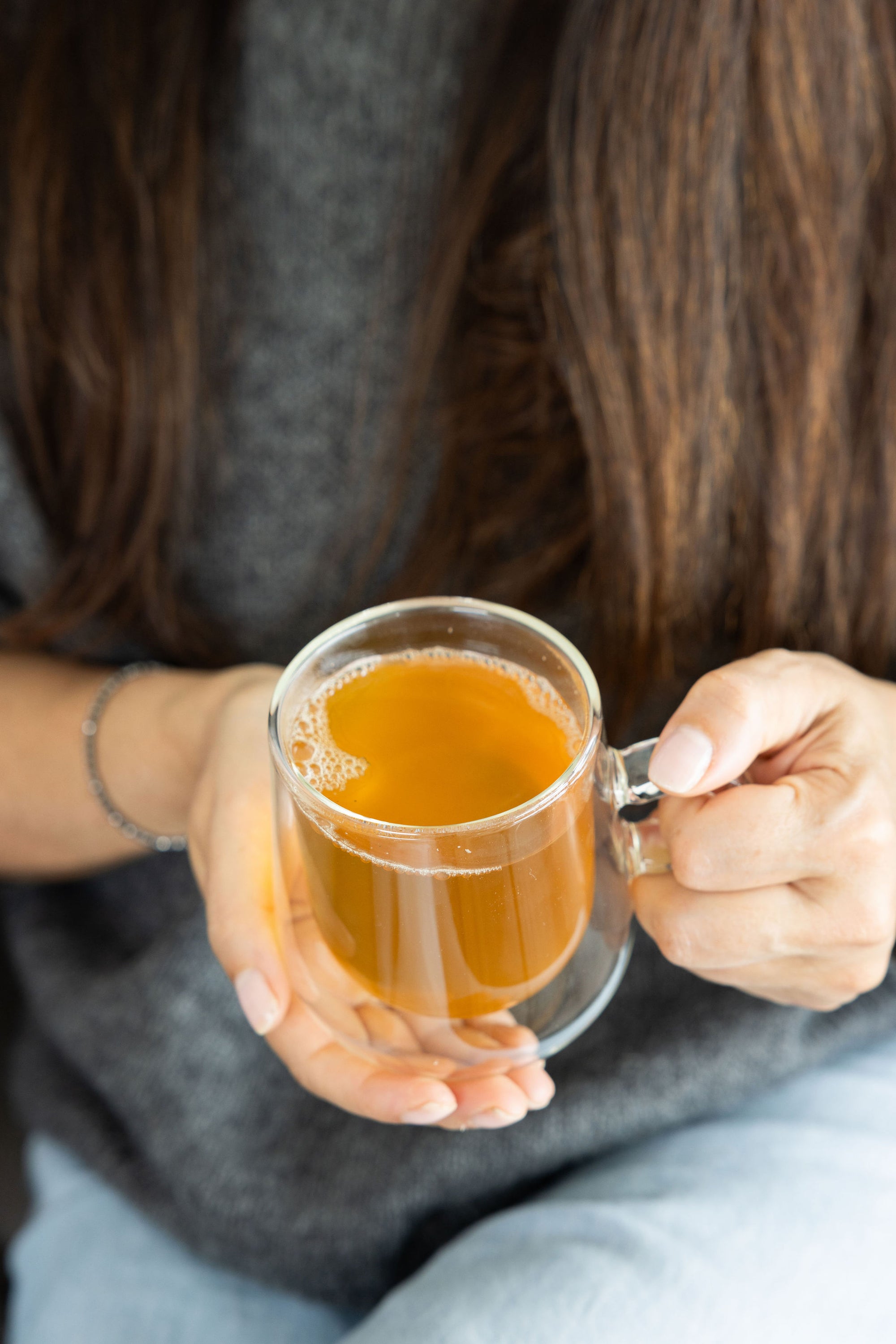 A girl holding a clear cup of warm golden Revive Tea from spritz wellness
