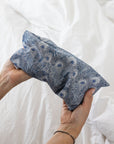 Hand holding a blue patterned eye pillow against a white background