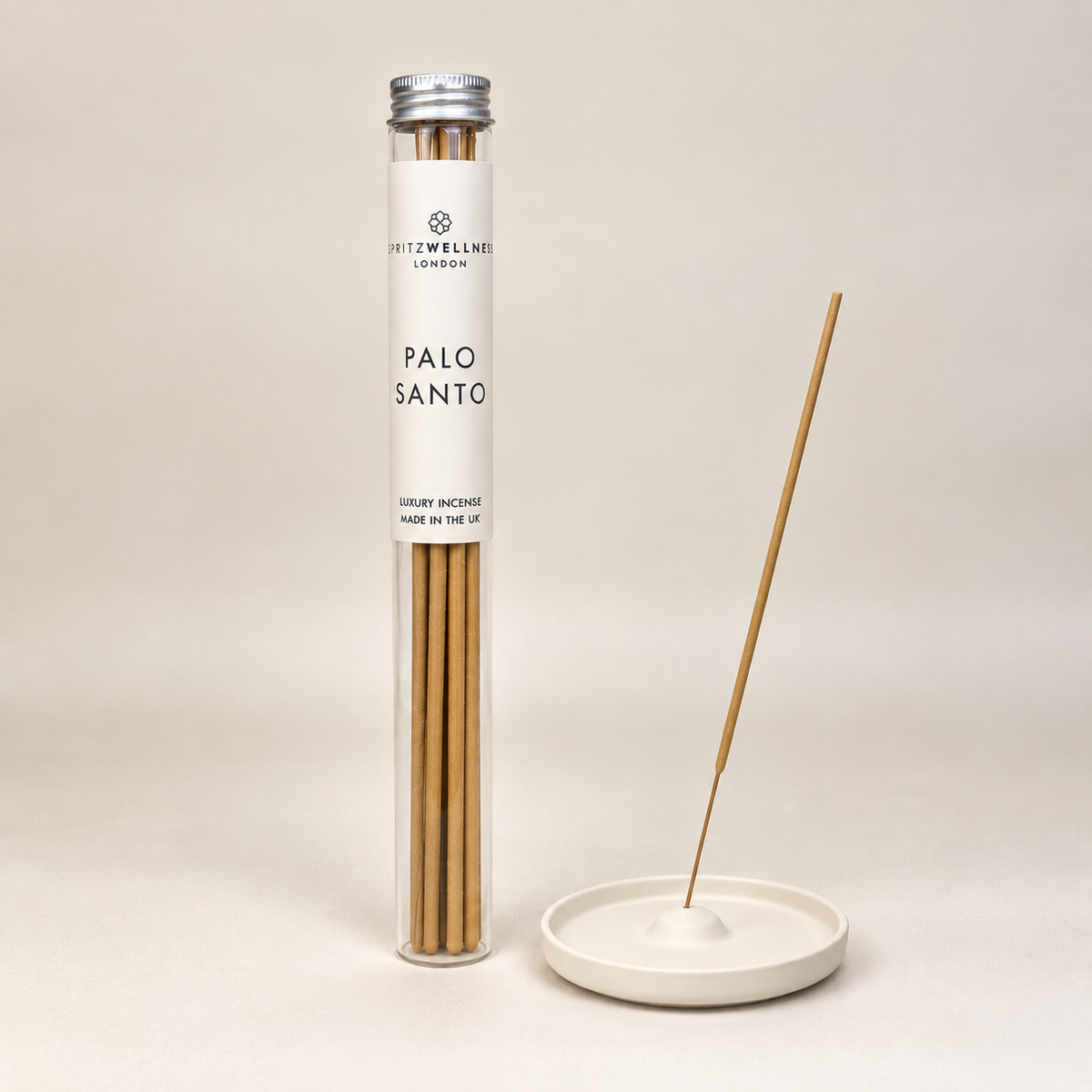 A tube of Hitzwell London Palo Santo incense sticks stands next to a small white ceramic incense holder on a warm beige background.