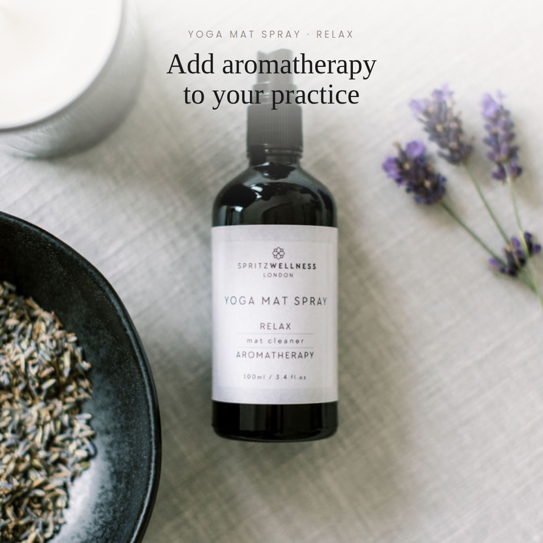 A bottle of Spritzwellness London Yoga Mat Spray in the 'Relax' scent, styled in a flat-lay arrangement with lavender flowers, a bowl of dried herbs, and a white mug on a textured white linen surface.